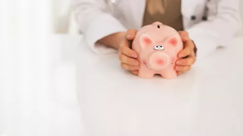 Doctor holds piggy bank.